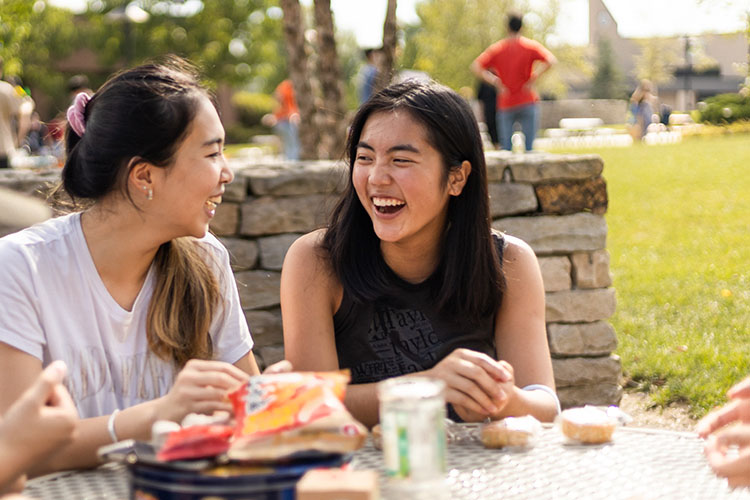 Two students sit together laughing while sharing a meal